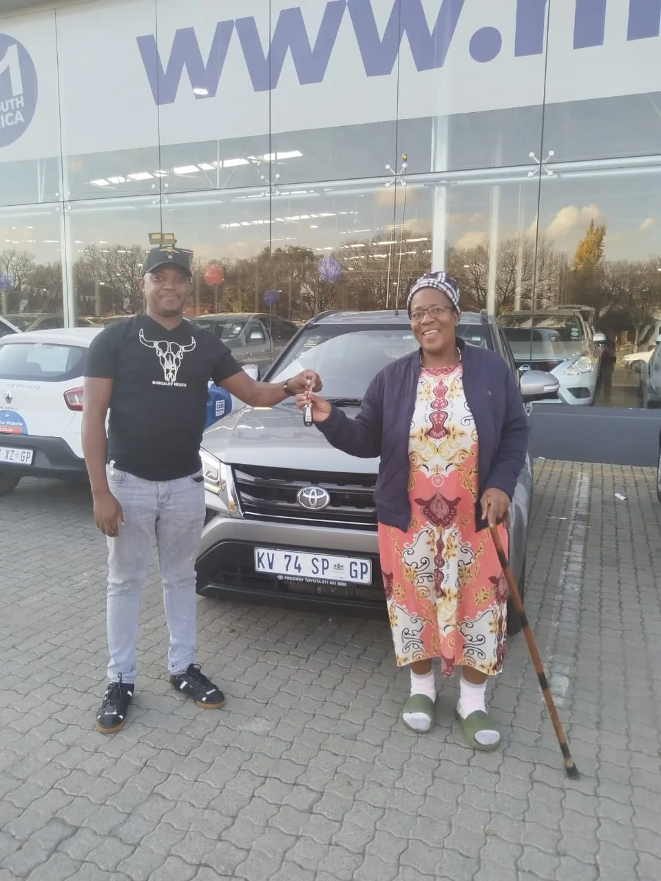 A happy customer receives the keys to her new grey Toyota SUV from a salesperson outside the dealership.