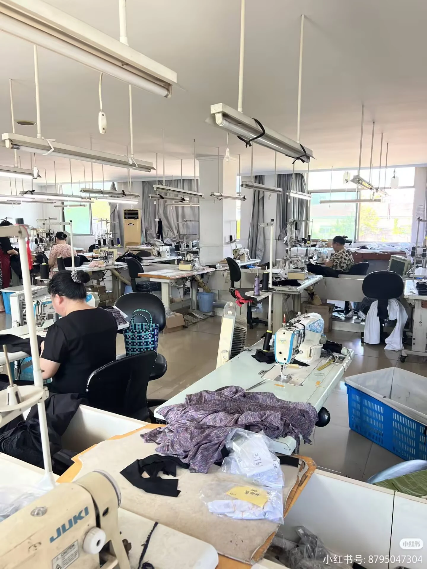 Rows of organised sewing stations and skilled production staff at a modern swimwear production facility, lit by natural daylight