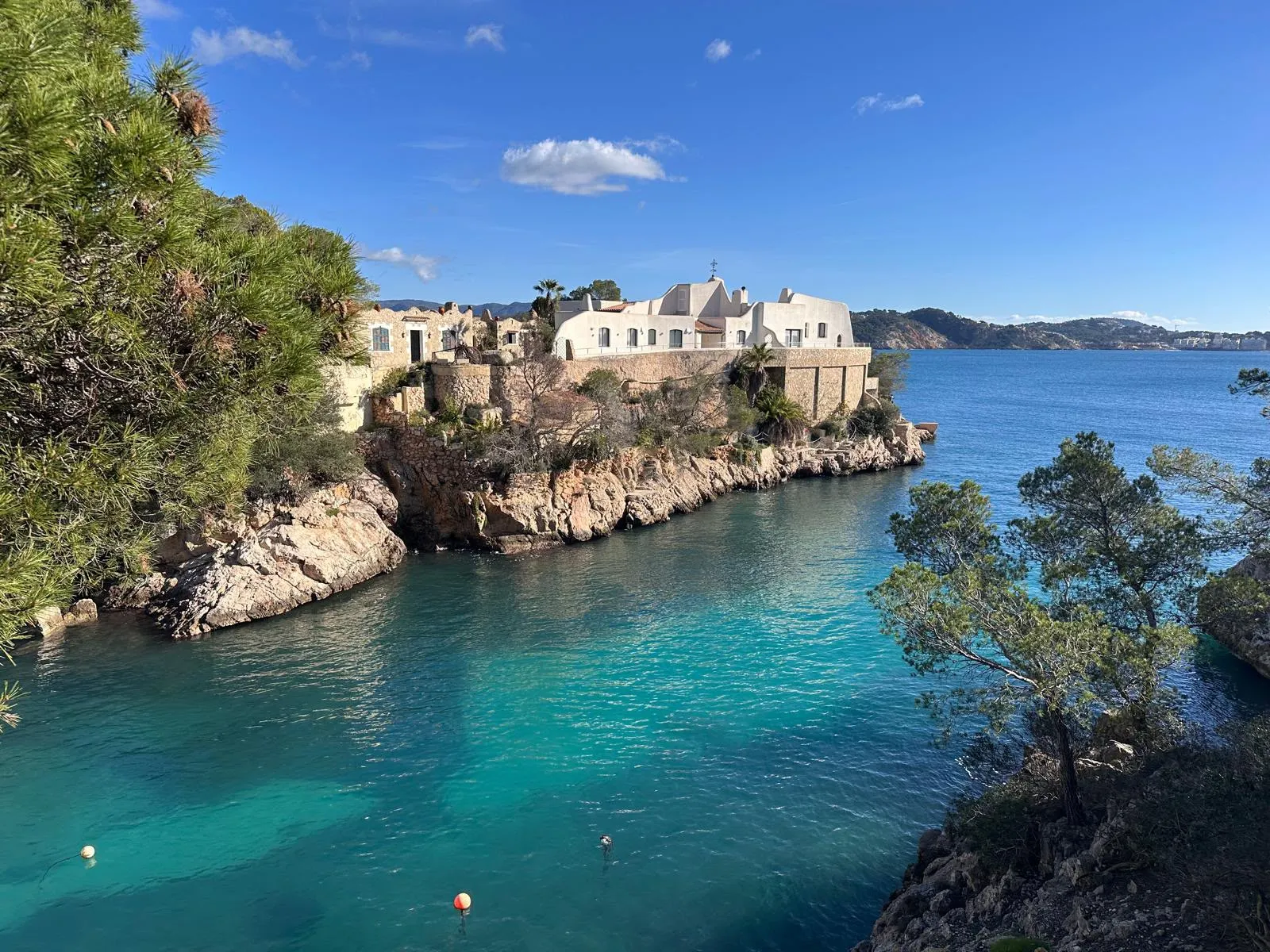 A cliffside cove on Mallorca — a whitewashed house above turquoise water framed by pine trees, one of the island's hidden corners