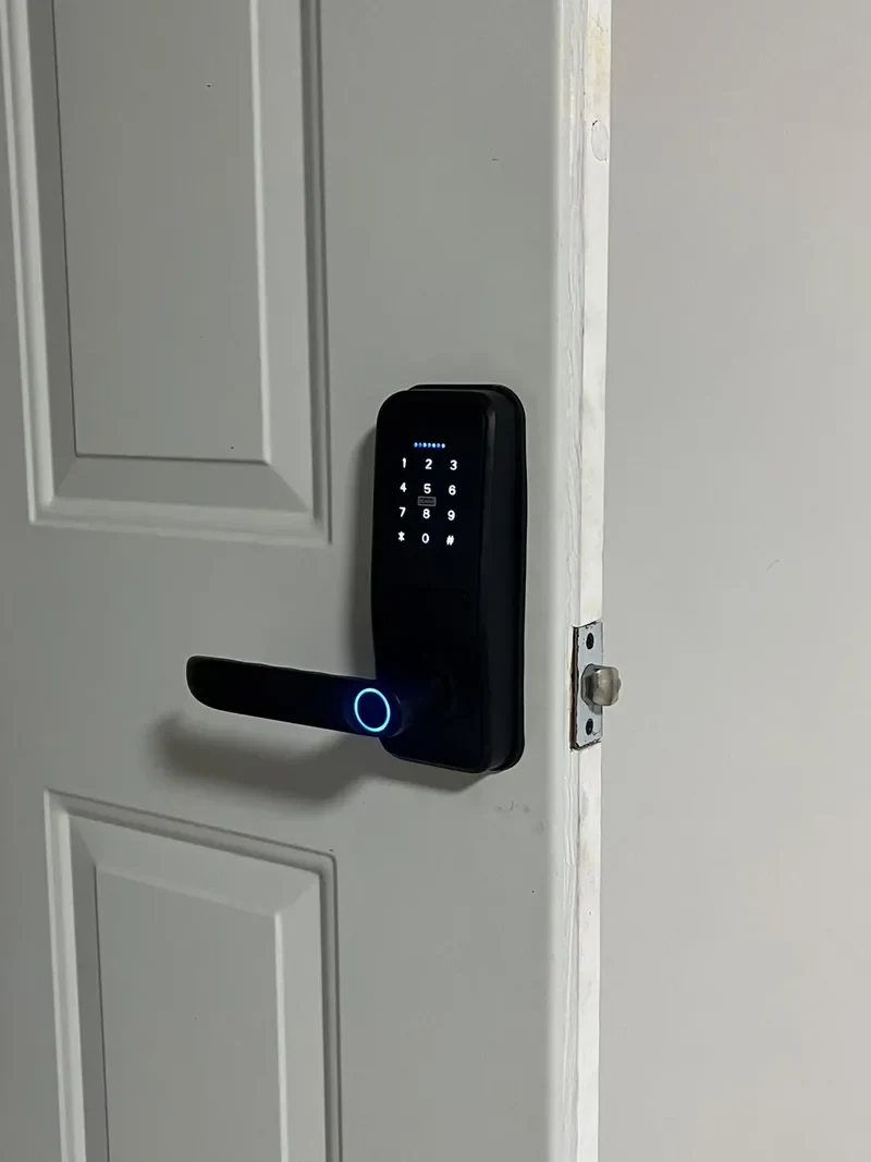 Cerradura inteligente negra con teclado numérico y lector de huella en una puerta blanca
