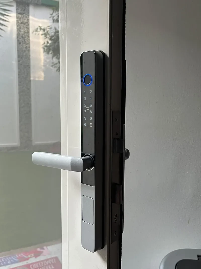 Cerradura inteligente delgada con teclado numérico y lector de huella en una puerta con vidrio