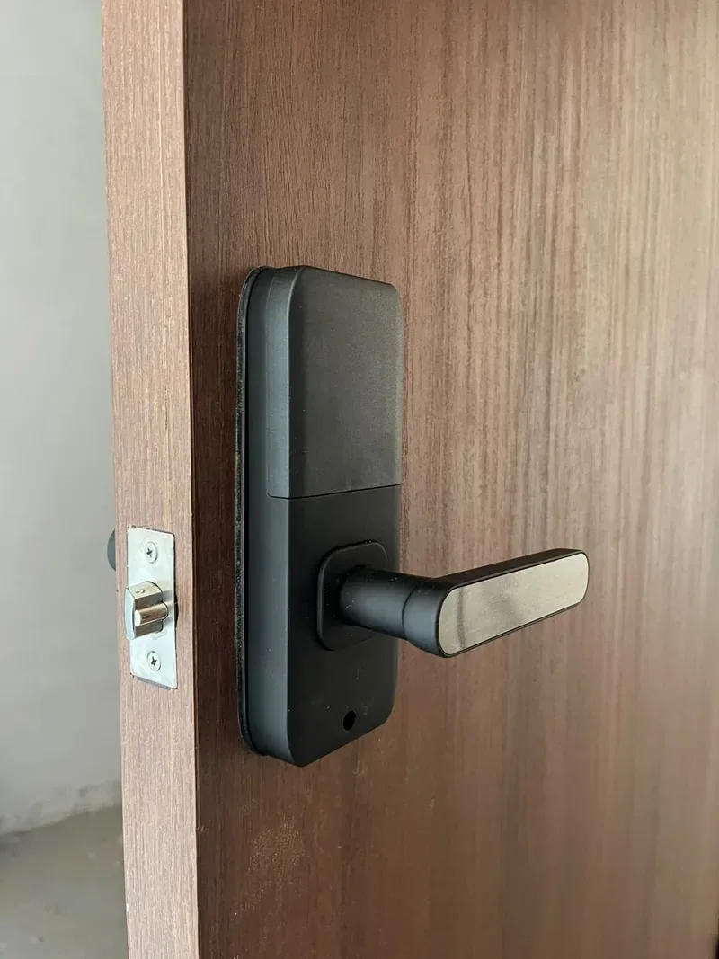 Cerradura inteligente negra con manija metálica instalada en una puerta de madera