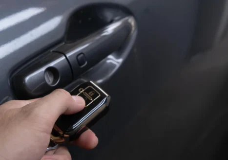 Mano con un control de llave de auto junto a la manija de una puerta de vehículo gris