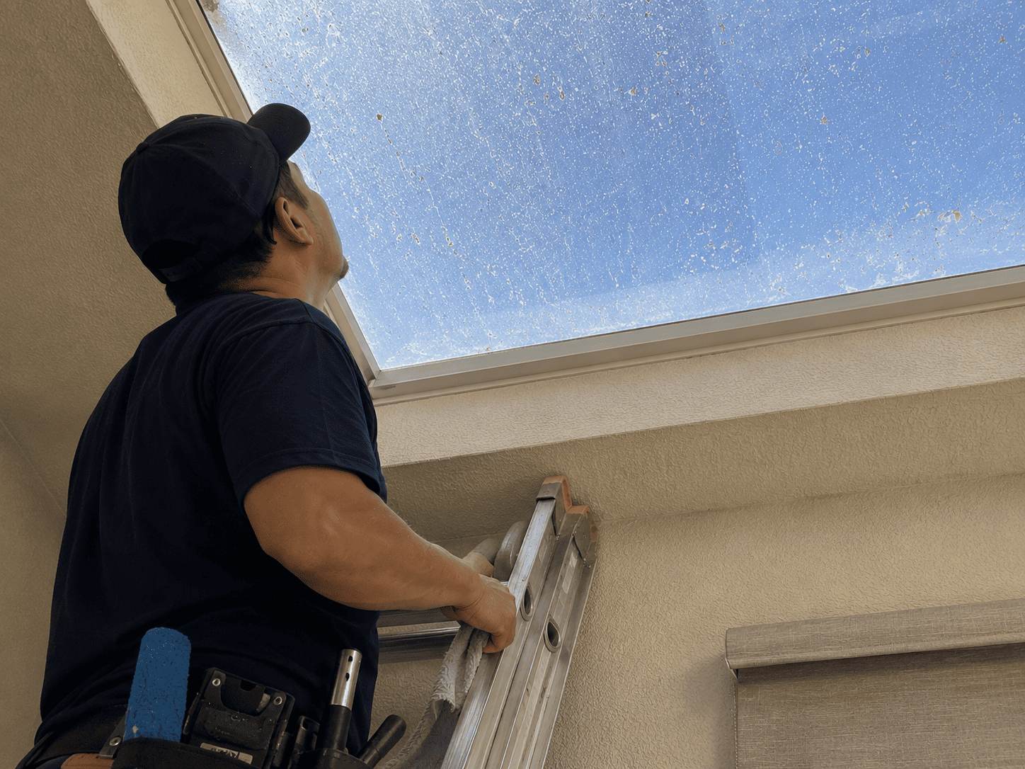 Professional window cleaner on a ladder inspecting a dirty skylight in Modesto, CA