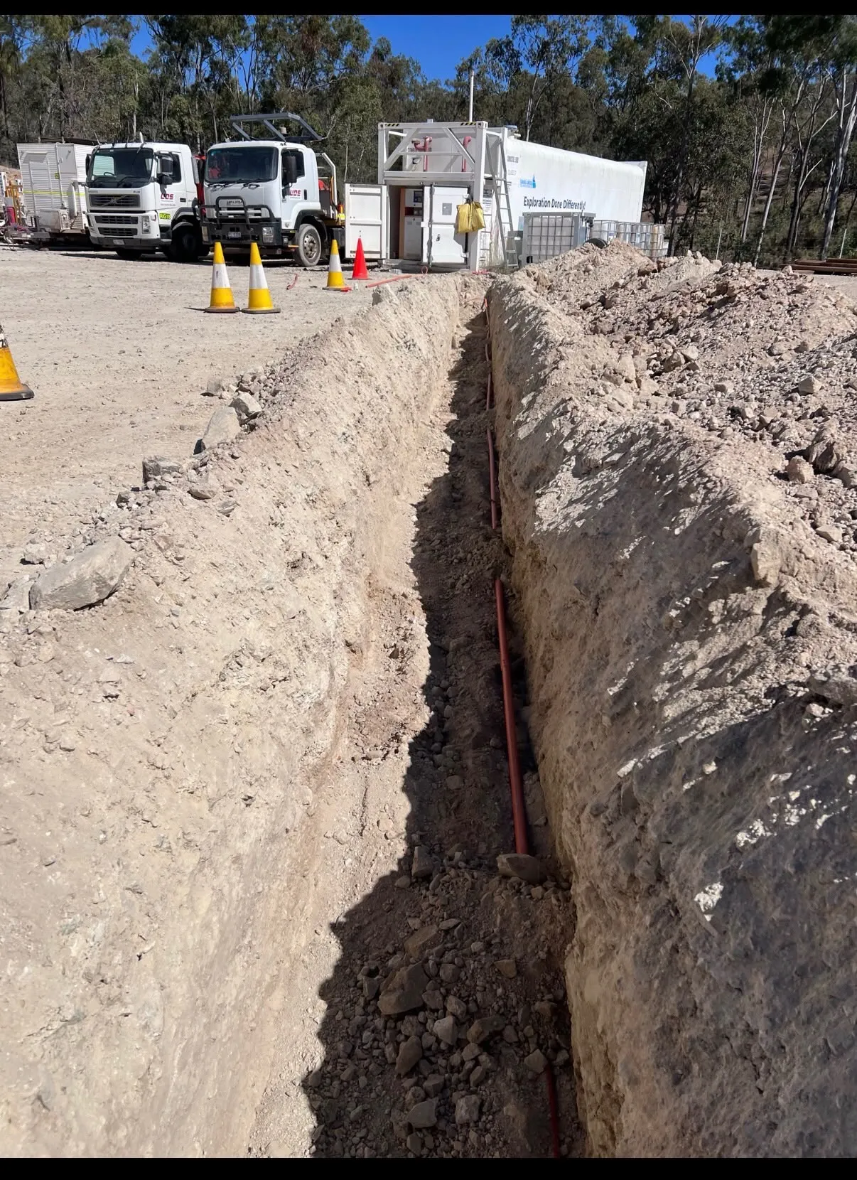 Underground electrical conduit laid in a deep commercial trench with site trucks in the background